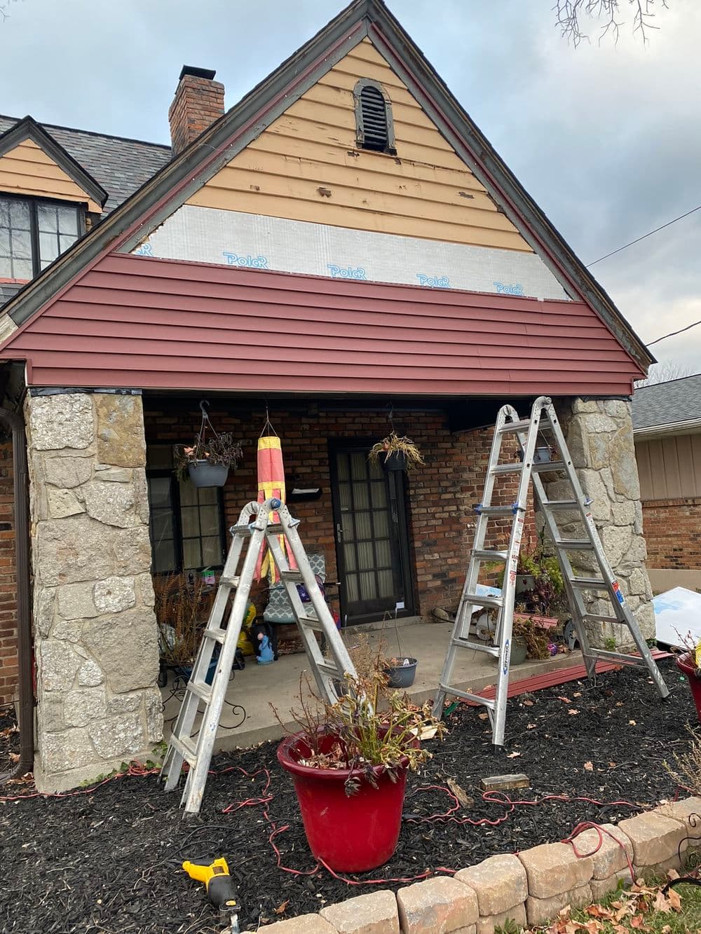 Home renovation featuring ladders, new siding installation, and a stone porch.